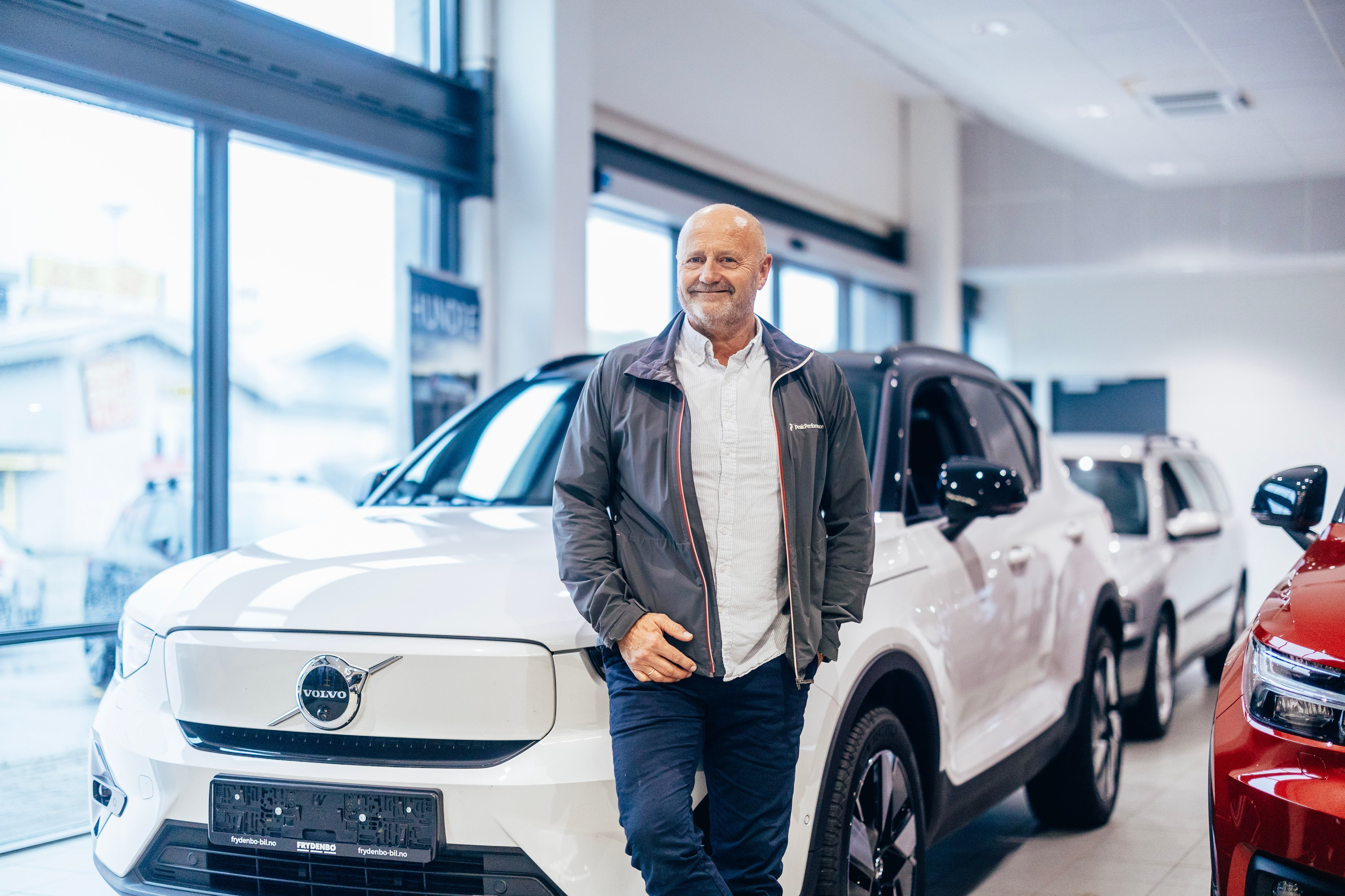 Smilende mann står fremfor en hvit Volvo EX40 i et bilsenter.